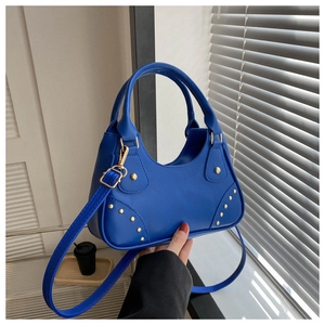 Dettaglio borsa in pelle blu acceso con borchie dorate e tracolla sottile rimovibile
