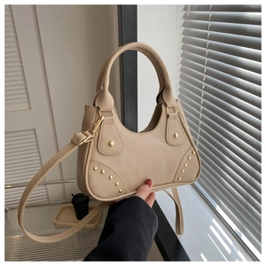 Dettaglio borsa a mezzaluna beige con borchie dorate e texture PU in luce naturale
