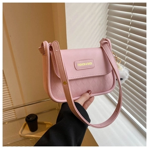 Detailed macro view of pink quilted handbag with gold brand plaque and plush pompom charm