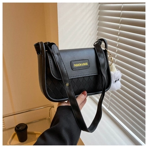 Detail of black quilted shoulder bag featuring a plush doll charm and brand logo plate