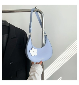 Détail du sac sous le bras en forme de croissant bleu clair avec charm fleur et logo