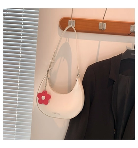 Detail einer weißen Mondsichel-Schultertasche mit rotem Blumenanhänger und Markenlogo