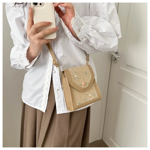 Close-up of straw woven crossbody bag with green flower embroidery and thin leather strap