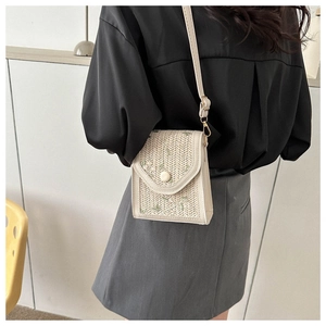 Détail d'un sac bandoulière tissé beige avec broderie florale porté par un mannequin
