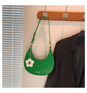 Nahaufnahme der smaragdgrünen Halbmond-Tasche aus Leder mit weißem Blumenanhänger