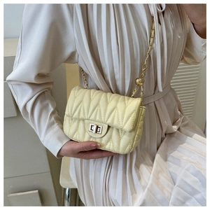 Close-up of quilted beige chain crossbody bag with metal lock worn by a model