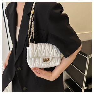 Close-up of white quilted chain bag with V-stitch pattern and gold metal lock on a model