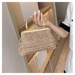 Detail einer handgehaltenen Stroh-Clutch mit goldenem Metallgriff und feiner Kette