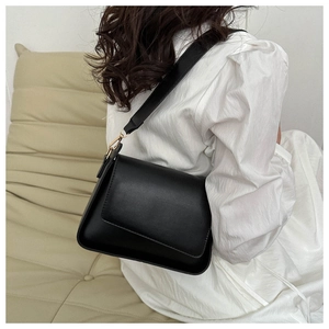 Close-up of a minimalist black crossbody bag with wide strap and gold hardware