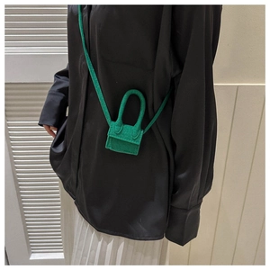 Detail view of a green mini crossbody bag styled on a model with a dark silk shirt