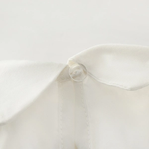 Detailed macro view of the white cotton shirt's sharp collar and small transparent button