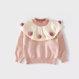 Close-up of pink knit sweater with white ruffled collar and purple pom-pom details
