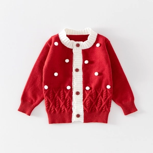 Détail du cardigan rouge en maille avec pompons blancs et motifs de torsades