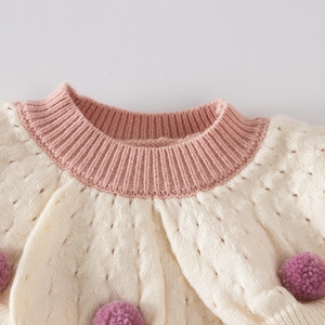 Close-up of baby girl knitted sweater with pink ribbed collar and pom-poms details