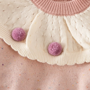 Detail of baby girl sweater with pointelle knit scalloped collar and purple pom-poms