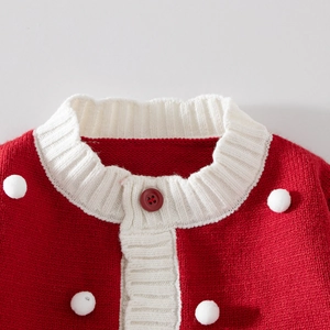 Détail d'un cardigan en tricot rouge pour fille avec pompons blancs et col contrasté