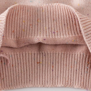 Detailed close-up of pink flecked knit fabric and elastic ribbed hem on girls' sweater