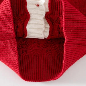 Détail d'un cardigan en tricot rouge avec des torsades et des poignets blancs côtelés