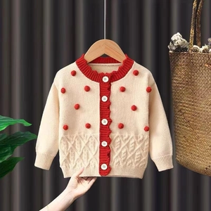 Détail du cardigan en maille avec pompons rouges et ourlet torsadé pour tenue de Noël enfant