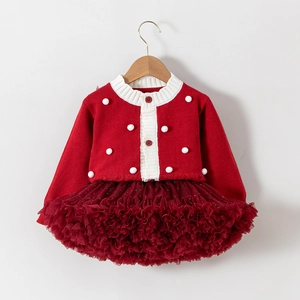 Détail d'un cardigan en tricot rouge à pompons et d'une jupe tutu en tulle multicouche