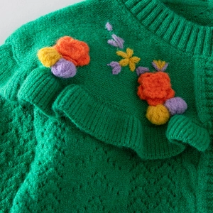 Detail of green knitted cardigan with ruffled collar and 3D floral embroidery accents