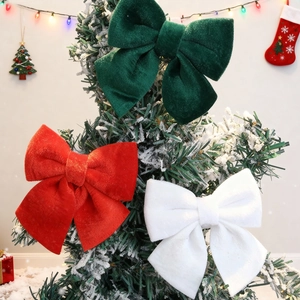 Three premium velvet Christmas bows in red green and white hanging on a snowy Xmas tree
