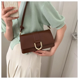Detail of a brown PU leather crossbody bag with a gold horseshoe buckle and slim strap