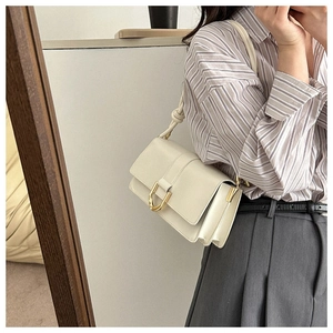 Detail of white PU leather flap bag featuring a metallic gold D-shaped buckle closure