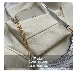 Close-up of silver crocodile texture and gold chain strap on the saddle underarm bag