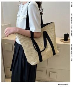 Straw tote bag with black canvas handles shown in a relaxed lifestyle shoulder carry pose