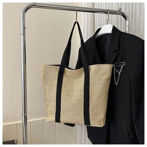 Detail of hand-woven beige straw tote bag with wide black canvas handles hanging on hanger