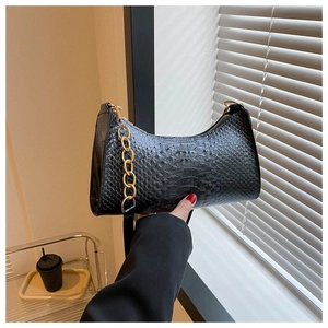 Close-up of black snakeskin embossed moon bag with gold chain strap in natural light