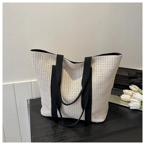 Detailed view of beige straw tote bag with black canvas straps on a wooden table