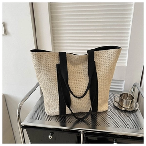 Detailed straw tote bag with black handles displayed on a minimalist metal shelf