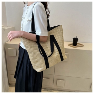 Detail of a large beige straw tote bag with black canvas straps on a female model