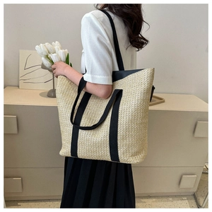 Fashionable straw tote bag with black strap detail carried by a model in a minimal setting