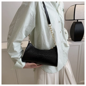 Detail of black crocodile texture underarm bag with gold chain strap on model