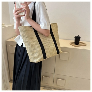 Detail of large woven straw tote bag featuring stylish black canvas strap accents