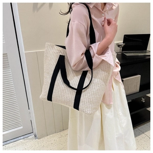 Straw tote bag with black canvas straps shown in a lifestyle casual setting