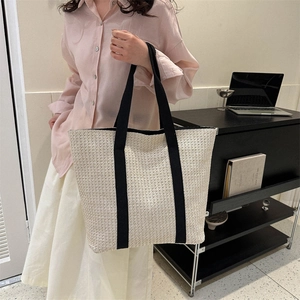 Fashionable beige straw tote bag with black wide straps shown on a model in a casual setting
