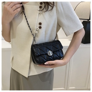 Close-up of black quilted shoulder bag featuring silver clasp and chain strap on model
