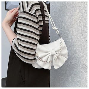 Detail of white leather shoulder bag featuring large bow and pearl chain strap decoration