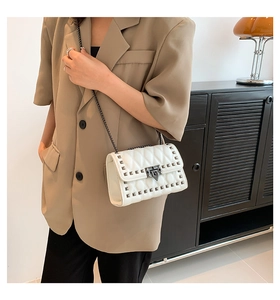 Detailed shot of white quilted shoulder bag featuring vintage studs and metal chain strap