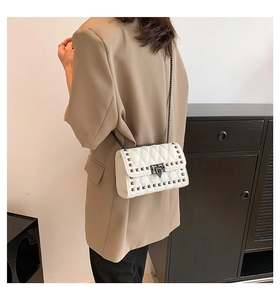 Quilted crossbody bag with silver studs and chain strap shown on model in home setting