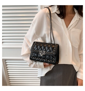 Quilted black crossbody bag with metal studs and chain strap worn in a lifestyle setting