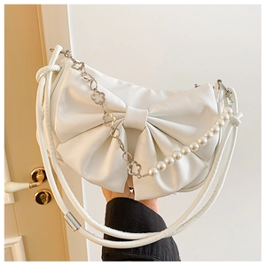 Detail view of bow-shaped off-white handbag with decorative pearl and floral chain