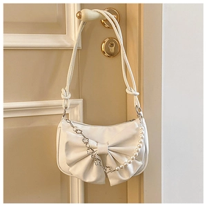 Detail of cream bow shoulder bag with pearl chain and floral metal strap on a door handle