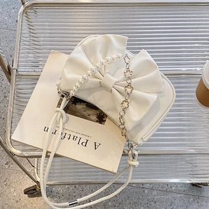 Chic white bow shoulder bag with pearl chain handle and flower detail on a magazine