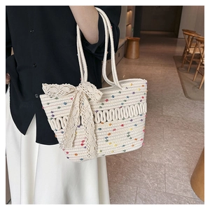 Detail of woven straw tote bag with colorful pom-poms and a large lace bow accent
