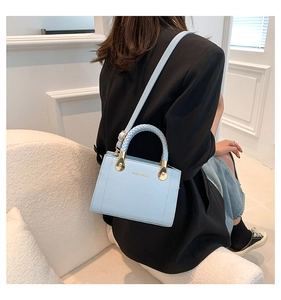 Détail de la poignée tressée bleu clair et du logo doré sur le sac à bandoulière élégant